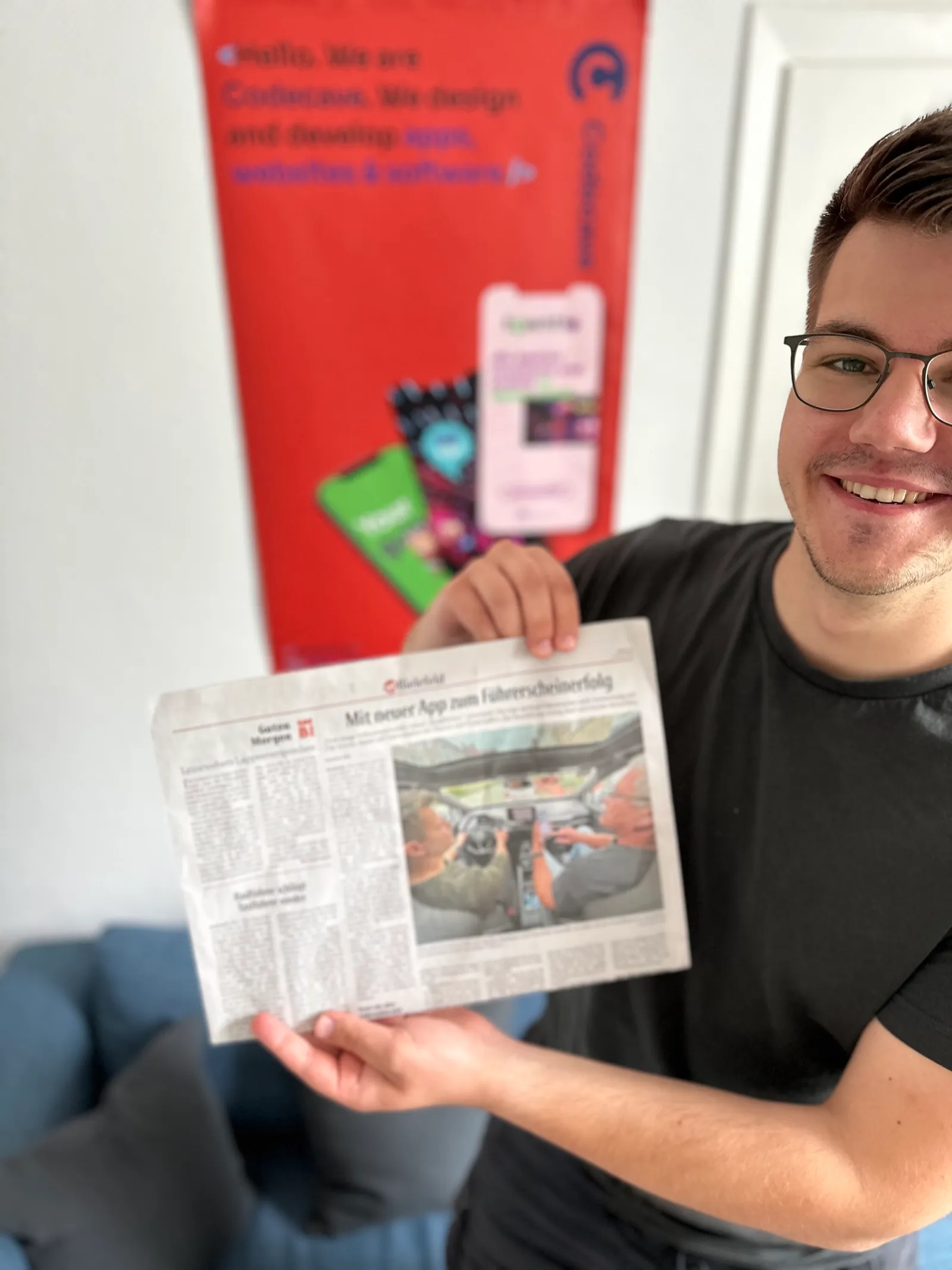 Aleksandar Jovanovic hält einen Zeitungsartikel über die App RoadReview vor dem CodeCave-Banner