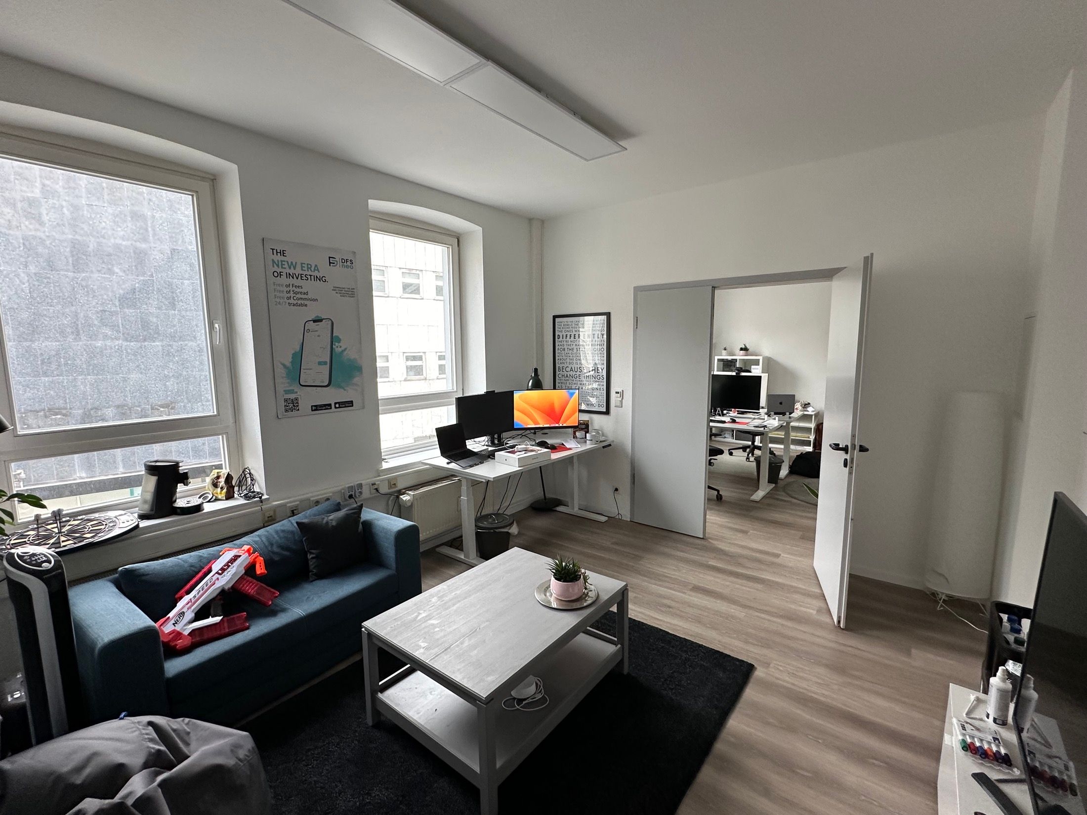 Office lounge area with a blue sofa and a view into the second workspace